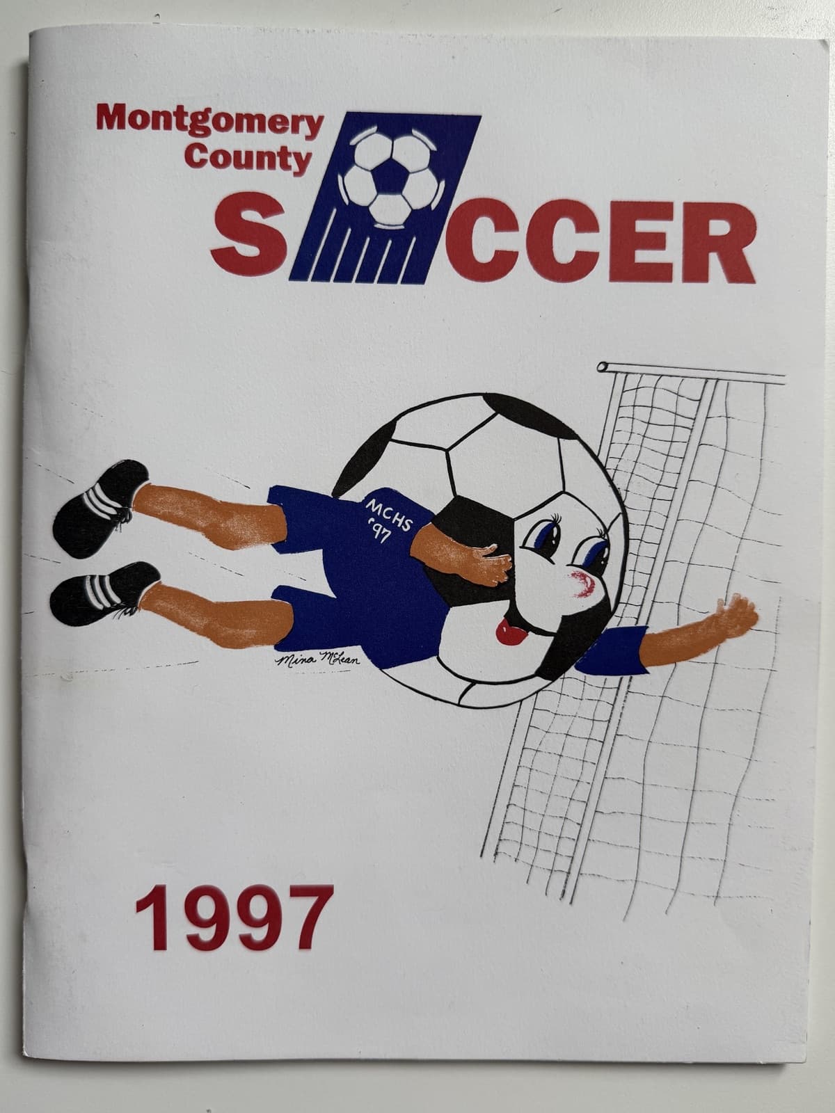 The hand-painted cover of the 1997 Montgomery County Soccer program: a cartoon player in an MCHS β97 jersey whose head is a giant soccer ball, diving full-stretch at the goal, beneath the βMontgomery County SOCCERβ wordmark and above a red β1997β